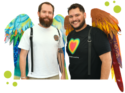 Two smiling men standing side by side, each wearing colorful, artistic wings