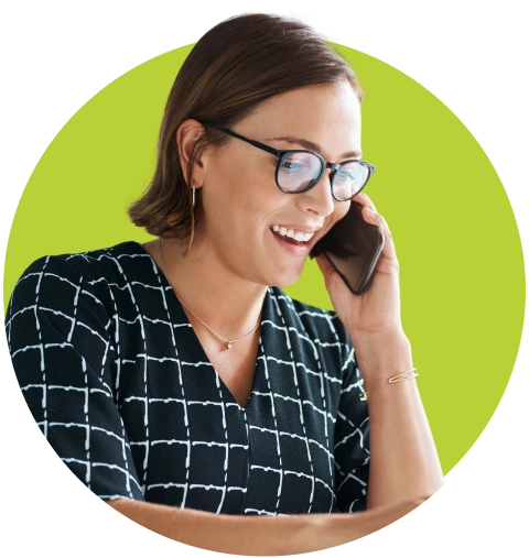 Smiling woman wearing glasses and a black checkered top, talking on a mobile phone, framed in a circular lime green background against a dark backdrop
