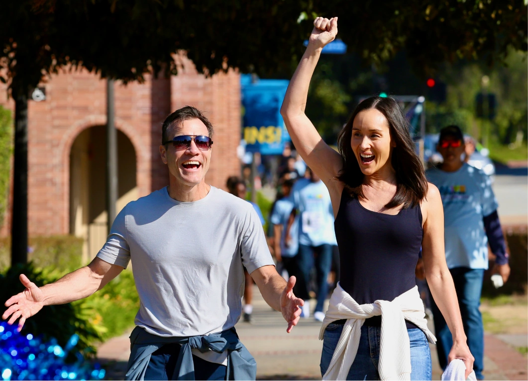 Smiling man and woman walking outdoors, celebrating with raised hands