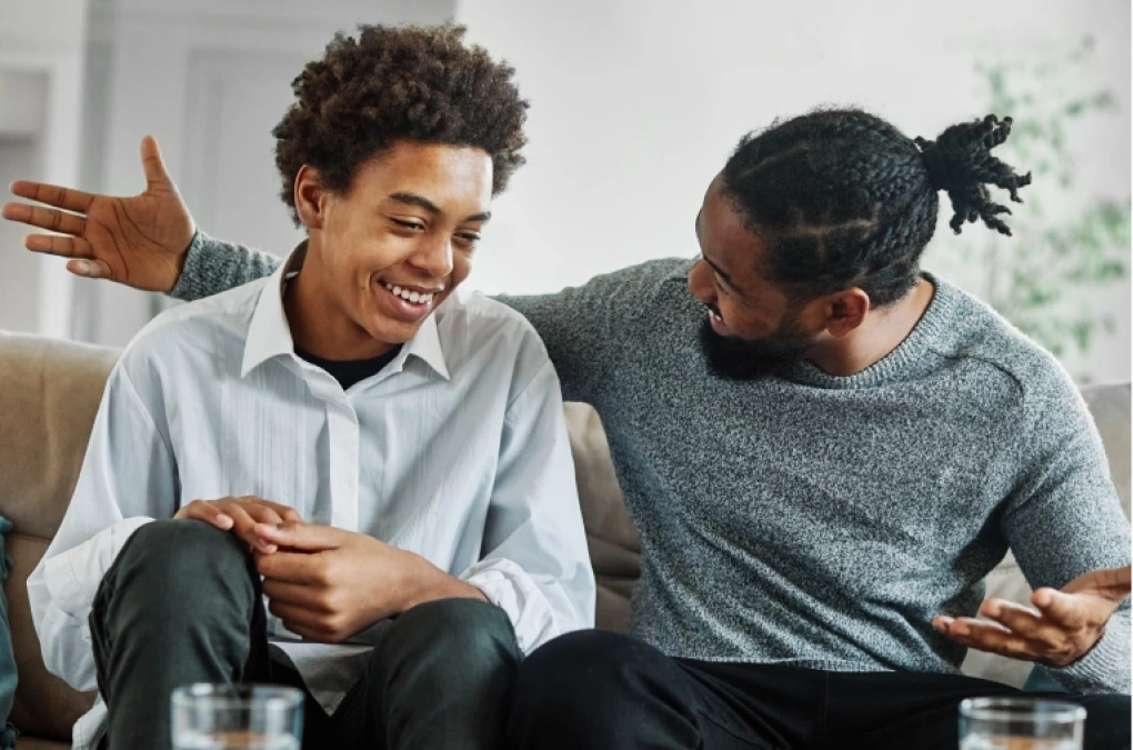 Two men smile and talk on a couch