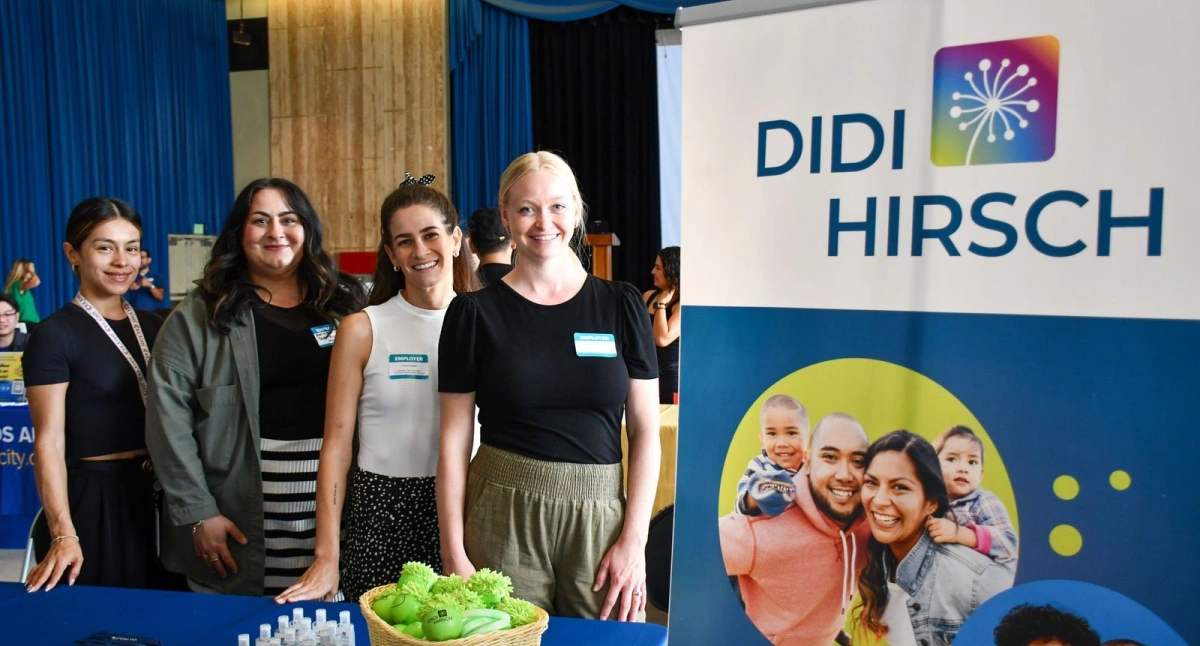 Group of people standing and smiling beside a Didi Hirsch banner at an event booth